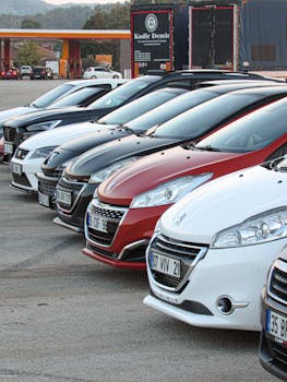 Lineup of modern cars neatly parked outdoors at a dealership with visible license plates.